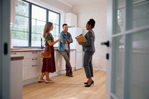 A smiling couple examines a home’s kitchen while an inspector points to features on a notepad.